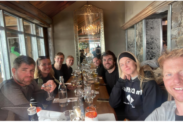a group of people on a long dinner table, the glasses are set and there are various alcoholic drinks 