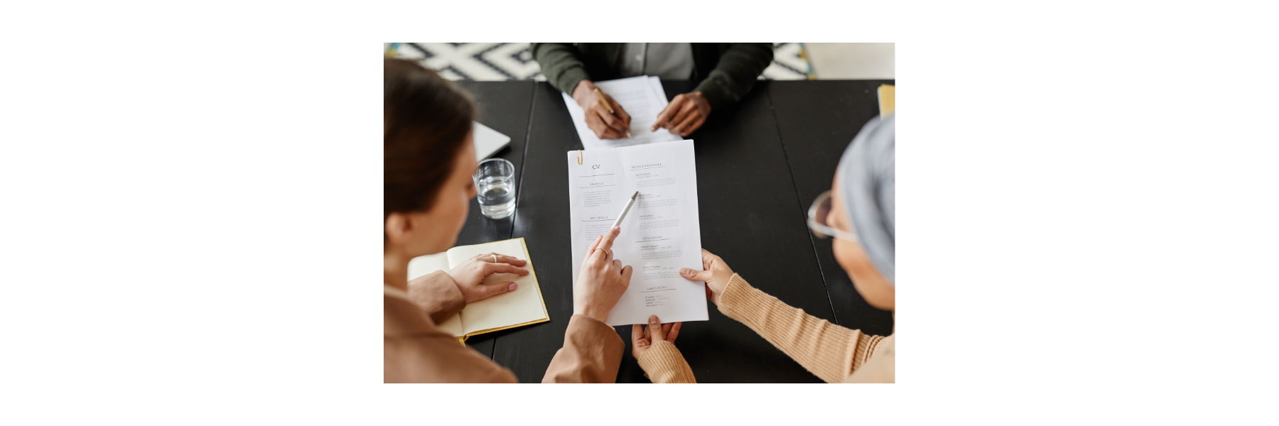 Two people are looking at a CV - there is a pen pointing to an area. 